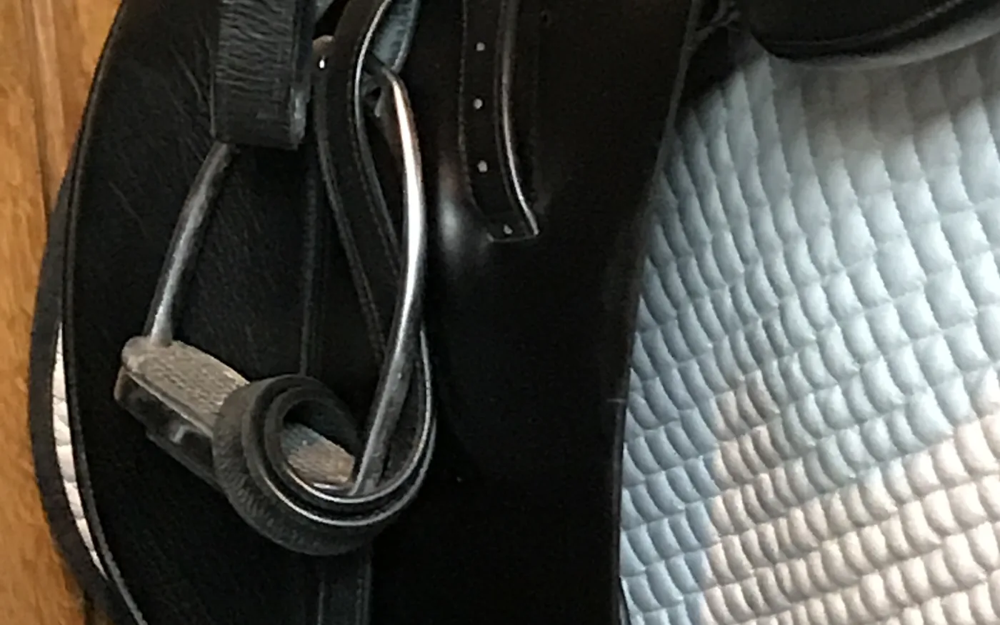 Detailaufnahme eines schwarzen Sattels mit hochgezogenem Steigbügel und heller Schabracke